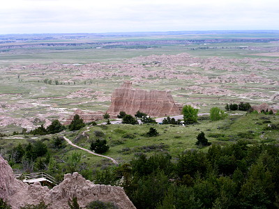 [A tall light-brown rock outcropping rises from the relatively flat green land around it. There is a light-colored trail through the green groundcover.]